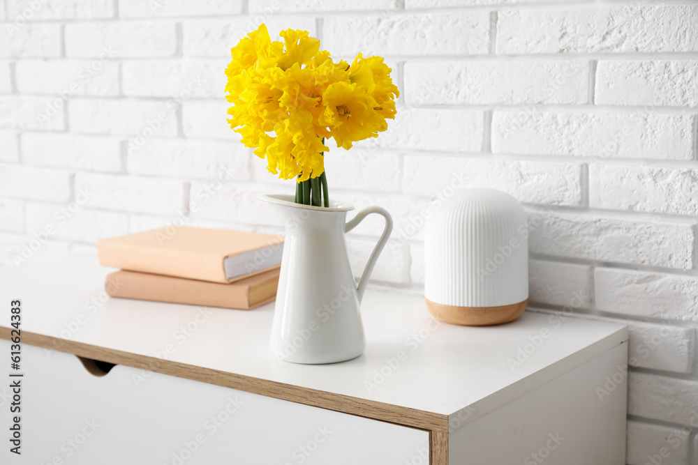 Vase with narcissus flowers and books on table near white brick wall