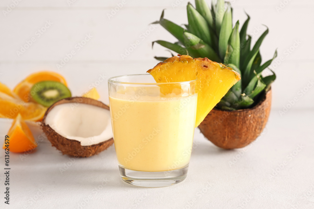 Glass of tasty pineapple smoothie, orange and coconut on table