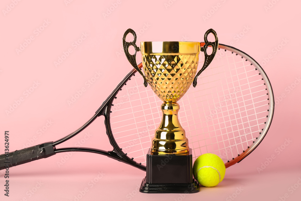 Gold cup with tennis racket and ball on pink background