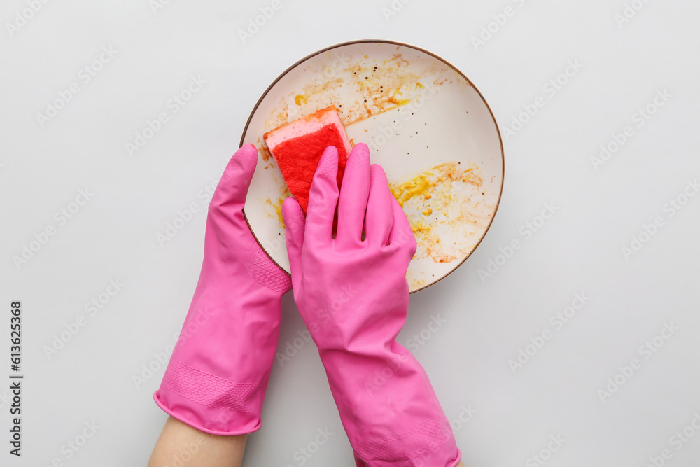 Female hands in rubber gloves washing dirty plate with sponge on grey background