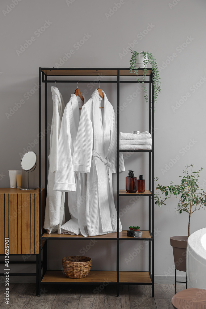 Shelving unit with bathrobes and bath accessories in interior of light room