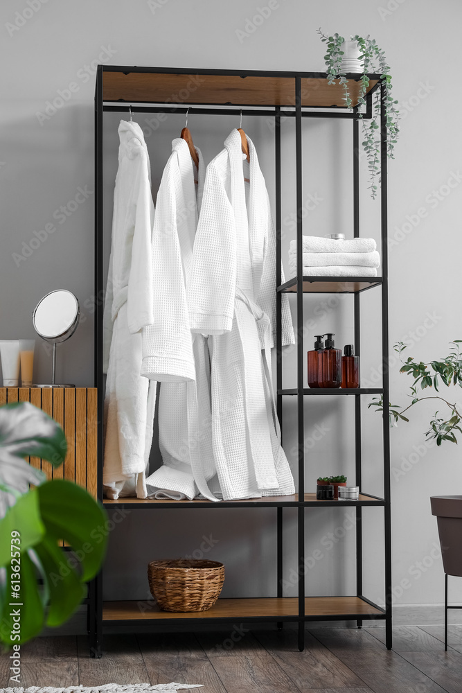 Shelving unit with bathrobes and bath accessories in interior of light room