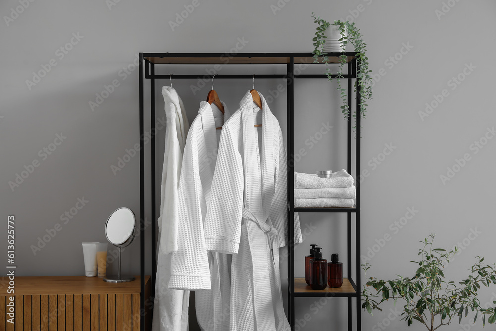 Shelving unit with bathrobes and bath accessories in interior of light room