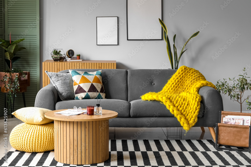 Interior of stylish living room with cozy grey sofa and reed diffuser on coffee table