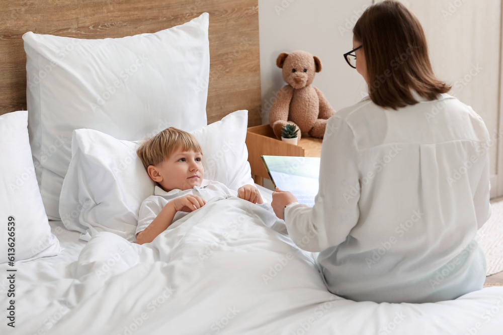 Nanny reading story to little boy in bedroom