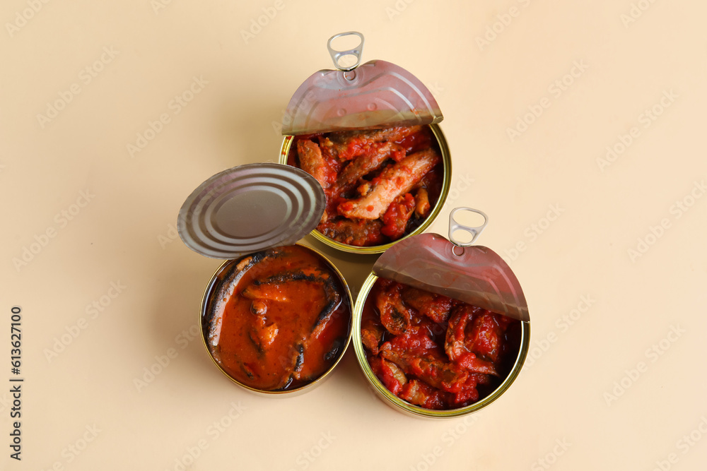 Opened tin cans with fish in tomato sauce on beige background