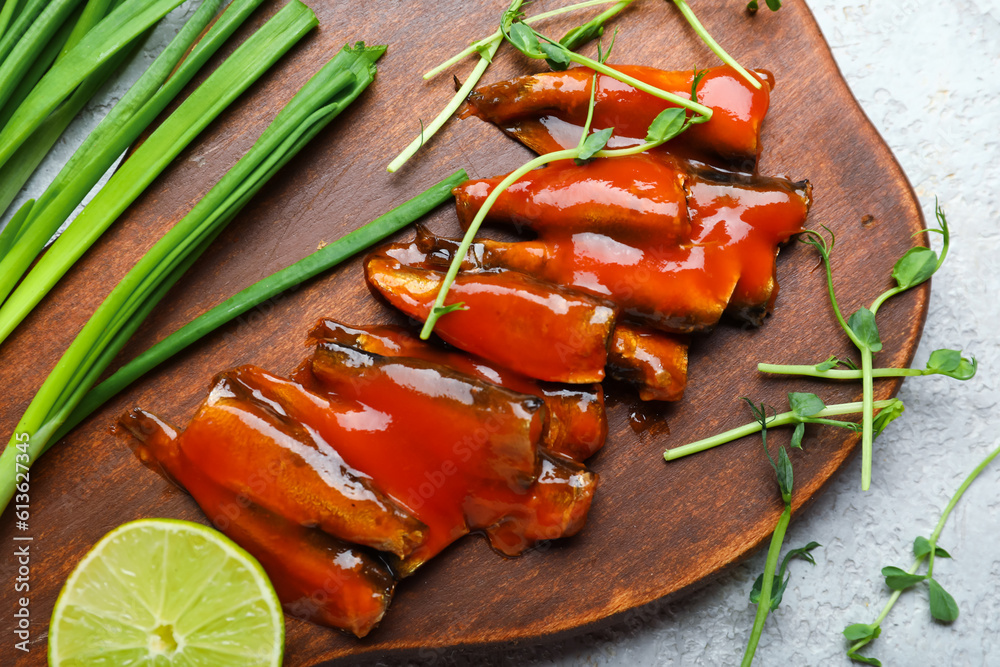 Board with canned fish in tomato sauce, lime, scallions and microgreens on grey table