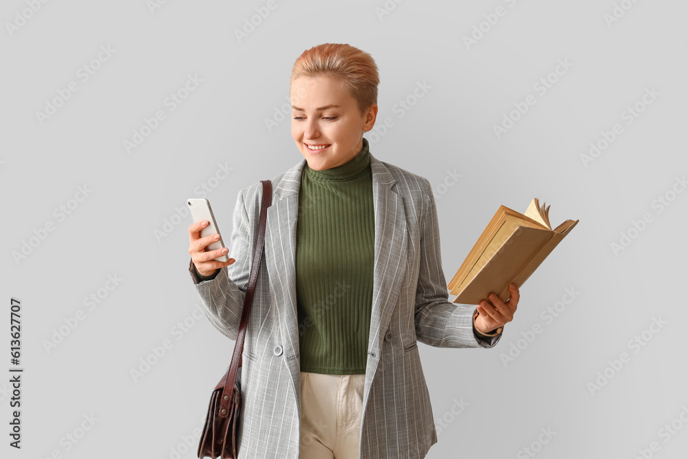 Female student with book and mobile phone on light background