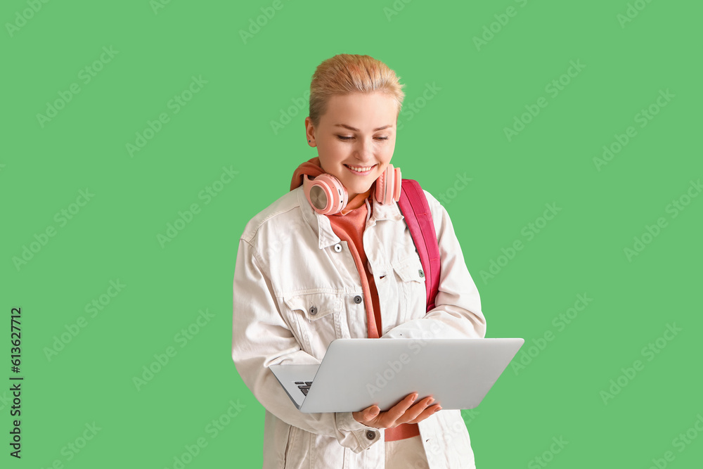 Female student using laptop on green background