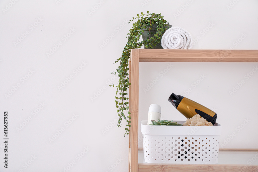 Shelving unit with bath accessories and houseplant near light wall