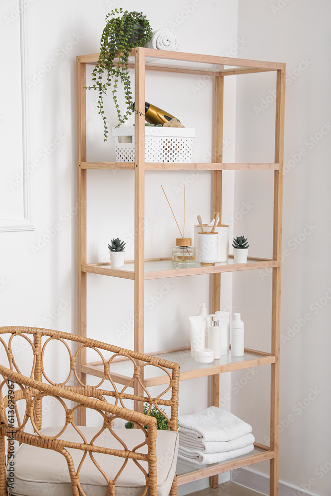 Shelving unit with bath accessories and houseplants near light wall