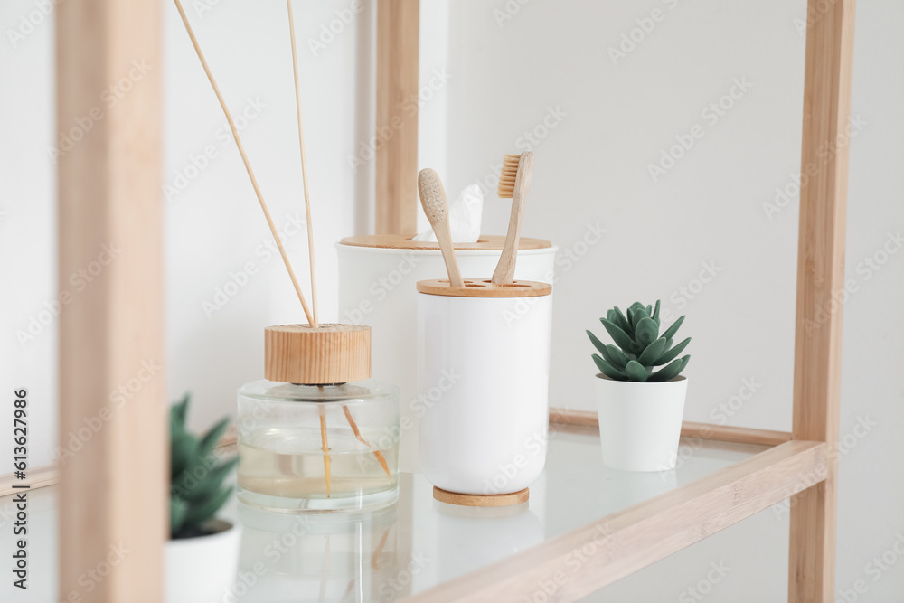 Bath accessories with reed diffuser and houseplants on shelf in light room, closeup