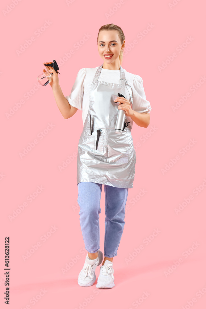 Female hairdresser with spray bottles on pink background