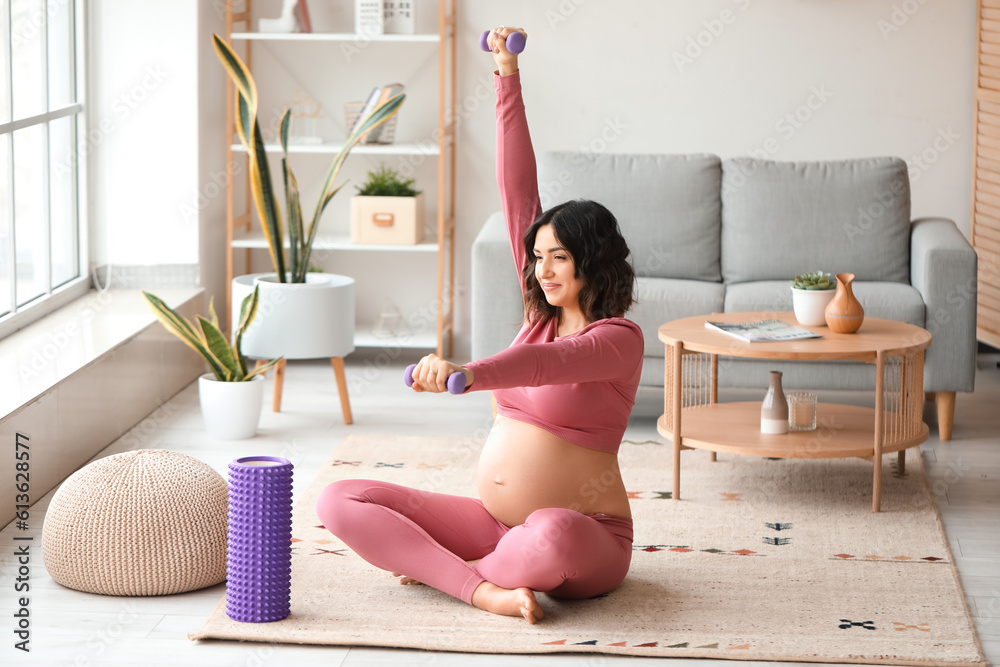 Sporty pregnant woman training with dumbbells at home