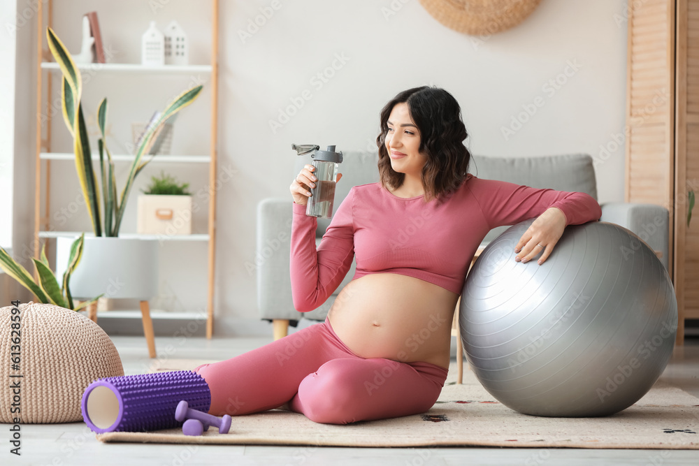 Sporty pregnant woman with bottle of water and fitball at home