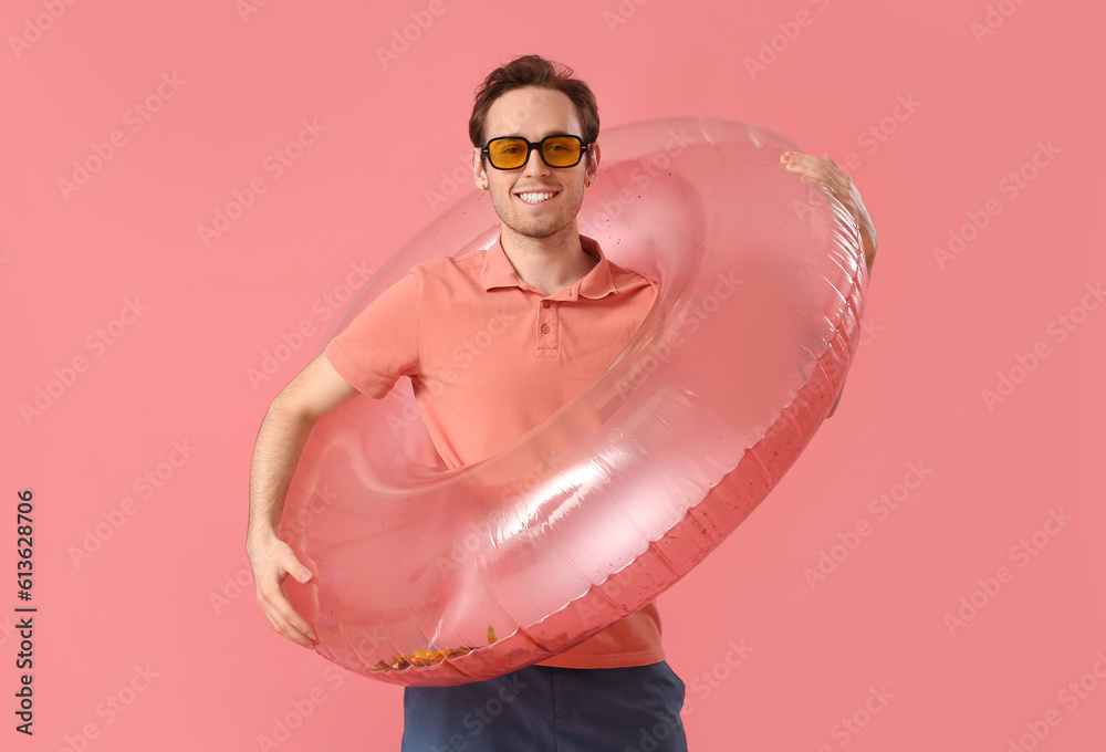 Young man with inflatable ring on pink background