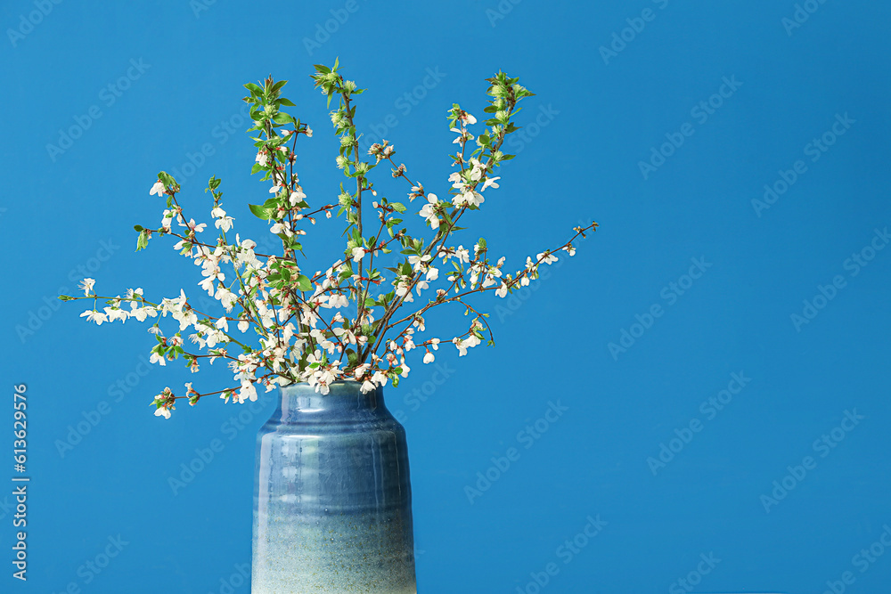 Vase with blooming tree branches on blue background