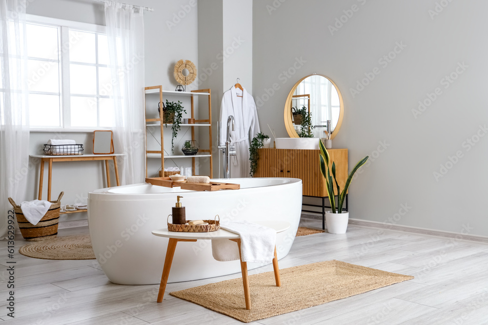 Interior of light bathroom with bathtub and bathing supplies on table