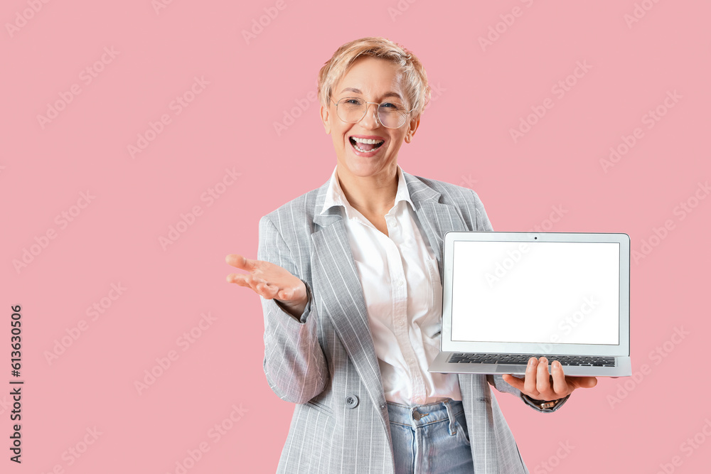 Mature female programmer with laptop on pink background