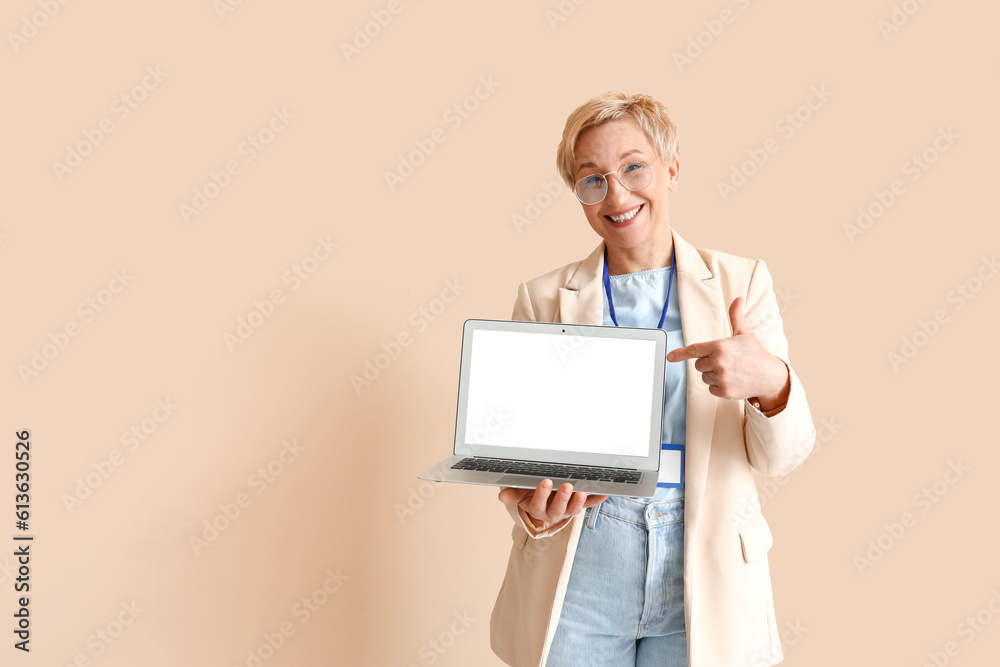 Mature female programmer pointing at laptop on beige background