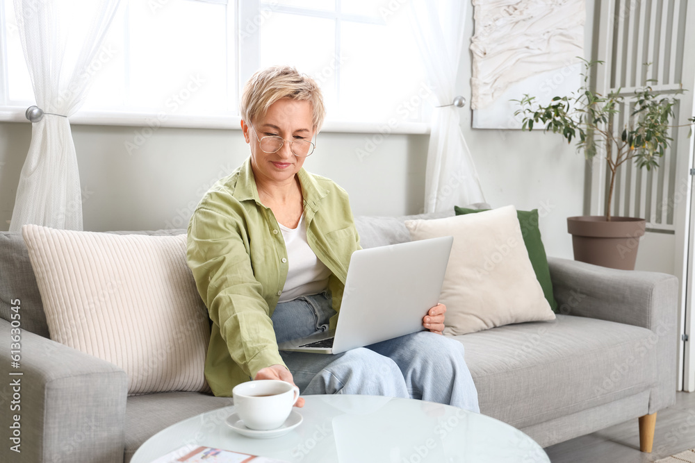 Mature female programmer working with laptop on sofa at home