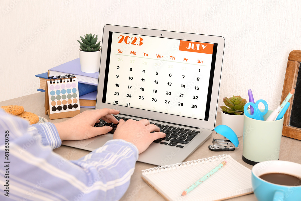 Woman using modern laptop with calendar at workplace