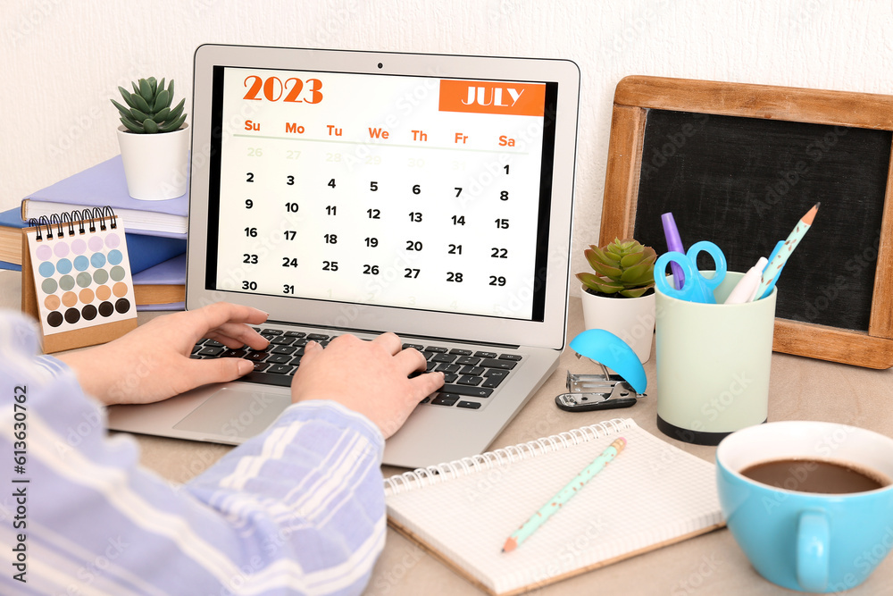 Woman using modern laptop with calendar at workplace