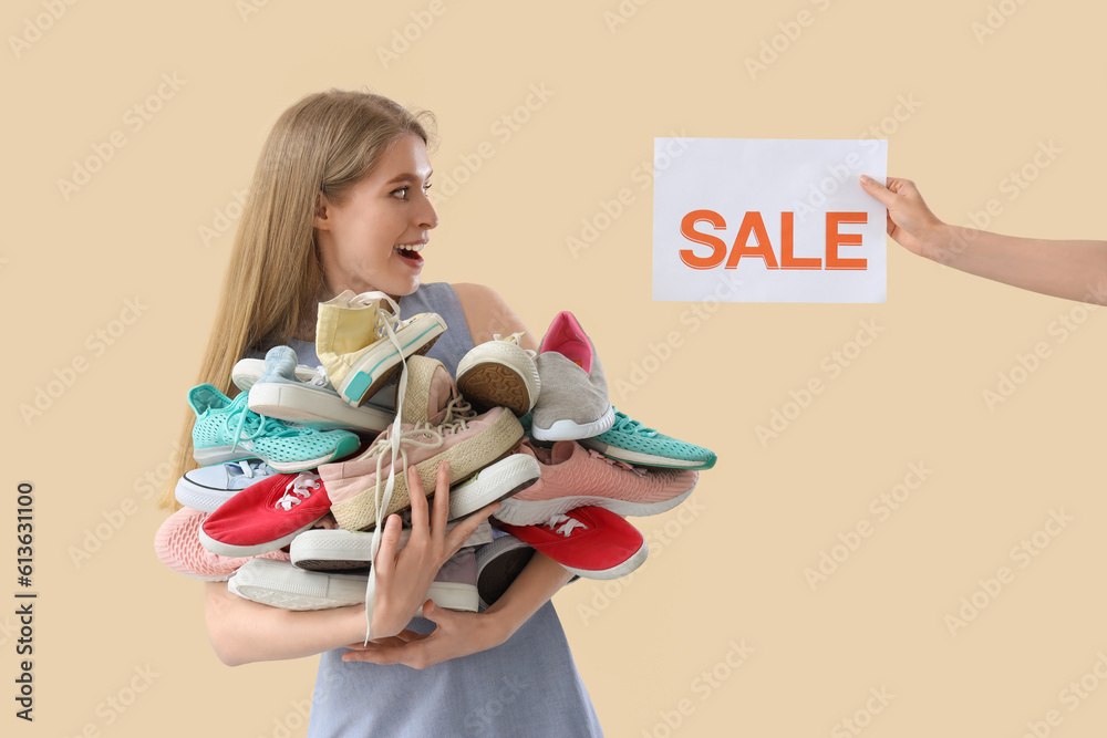 Happy young woman with shoes and sale sign on beige background