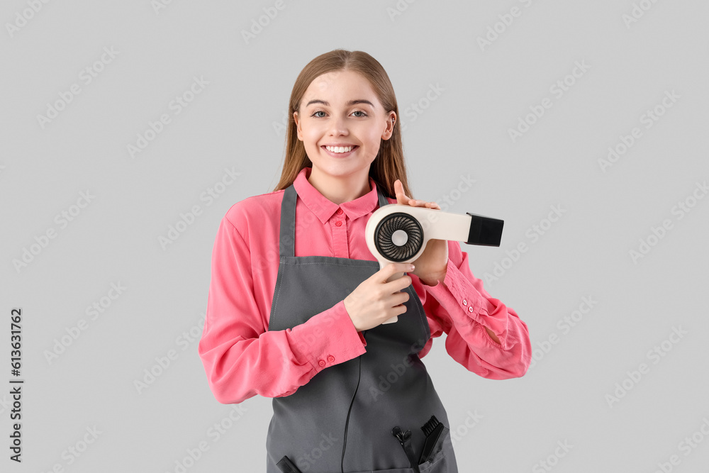 Female hairdresser with dryer on grey background