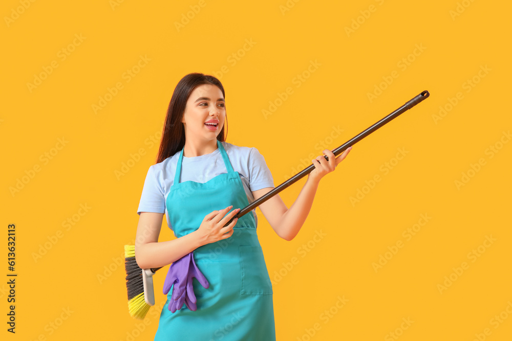 Female janitor with broom singing on yellow background