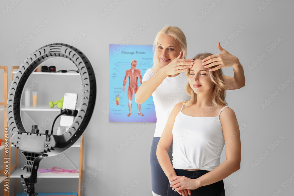 Female physiotherapist massaging face of young woman while recording video in rehabilitation center