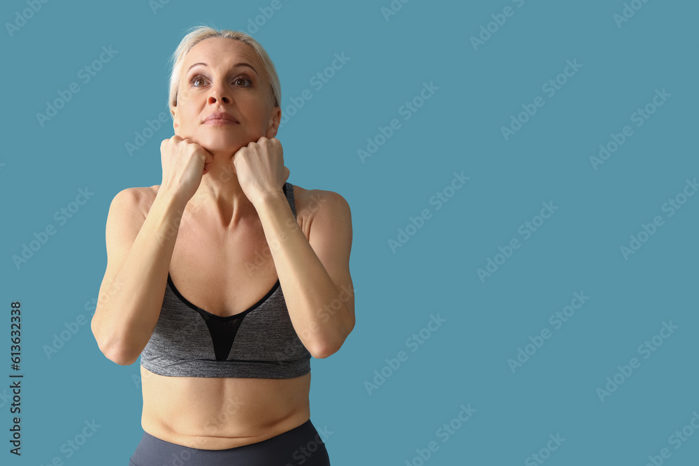 Sporty mature woman doing face building exercise on blue background