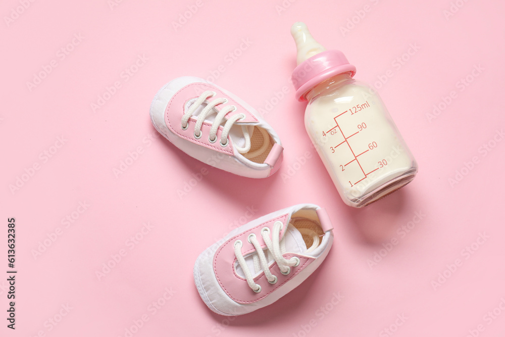 Bottle of milk for baby with booties on pale pink background