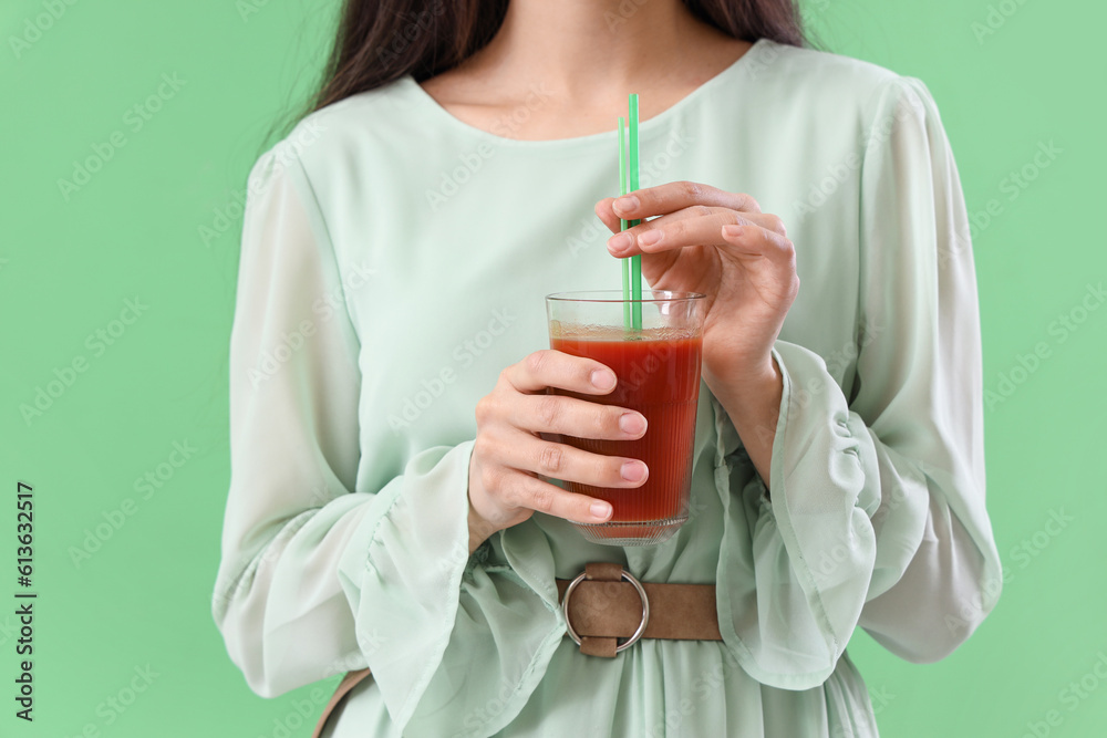 Young woman with glass of vegetable juice on green background, closeup