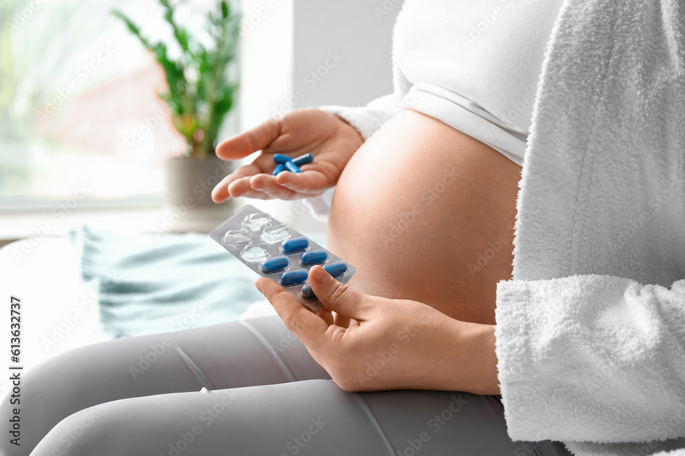 Pregnant woman with Folic Acid pills in bedroom, closeup