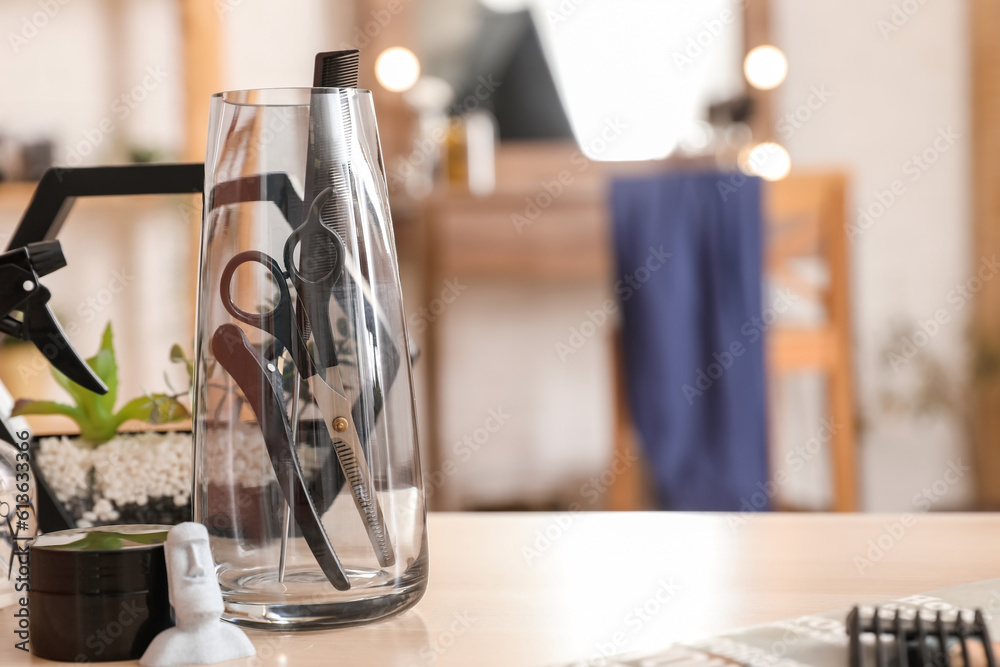 Glass with different hairdressing tools on table in beauty salon