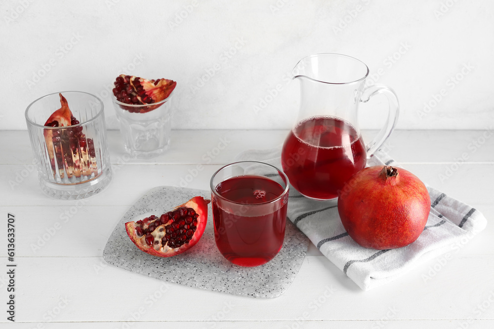 Jug and glass of fresh pomegranate juice on white wooden table