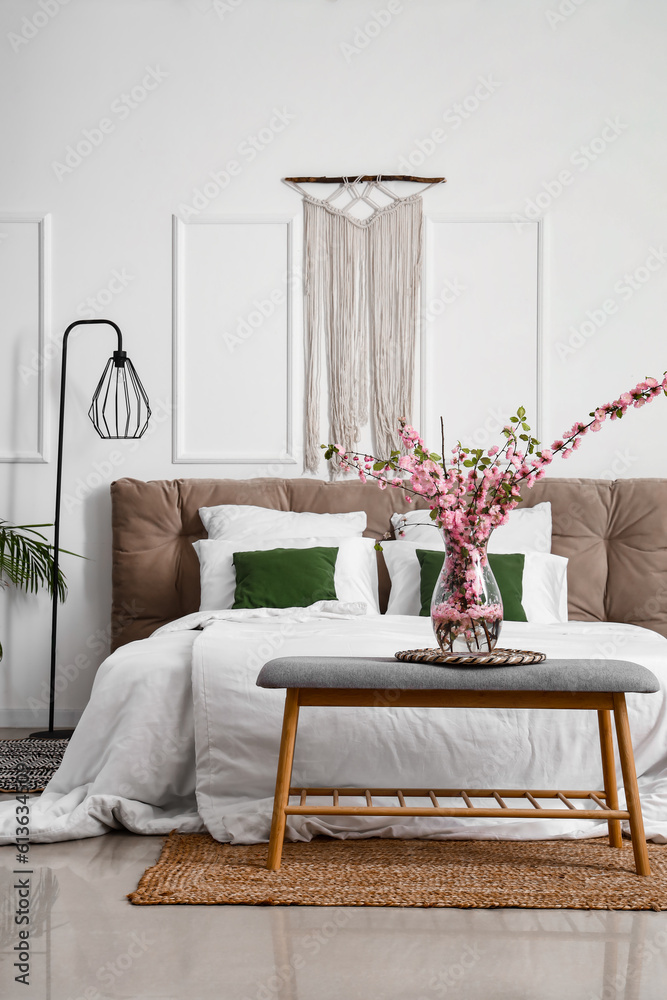 Interior of light bedroom with blooming tree branches on bedside bench