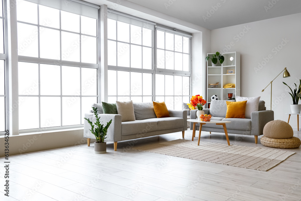 Interior of bright living room with sofas and tulip flowers on coffee table near big window