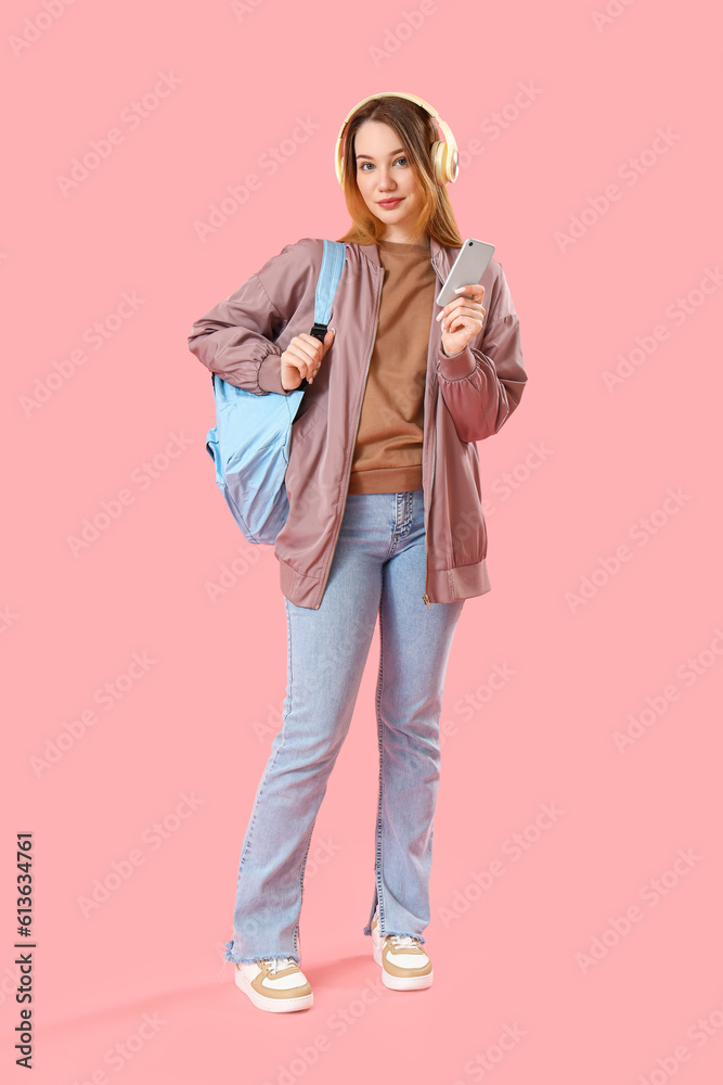 Female student in headphones with mobile phone on pink background