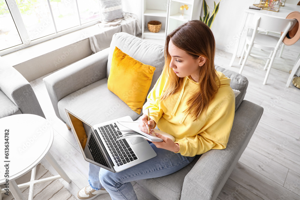 Female student studying with notebook and laptop at home