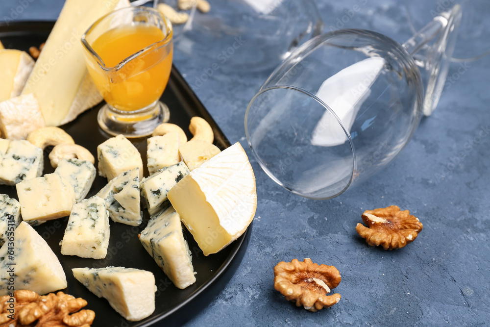 Tray with pieces of tasty cheese and wine glass on blue background, closeup