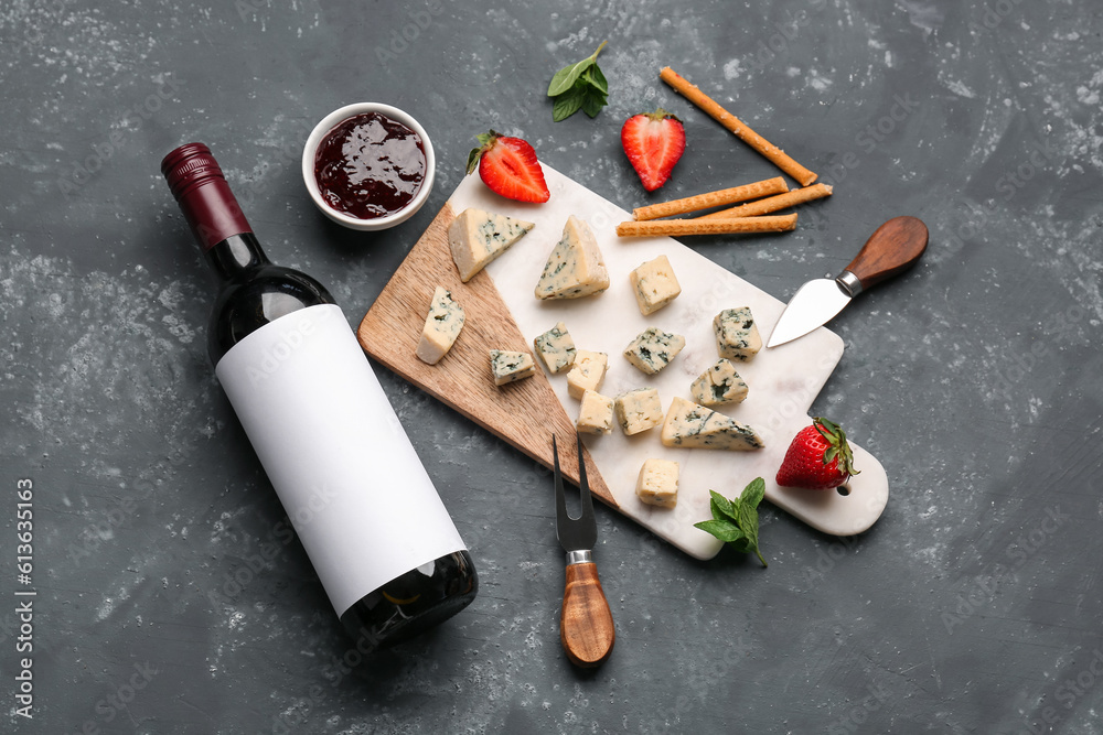 Pieces of tasty cheese, sauce and bottle with wine on grey background