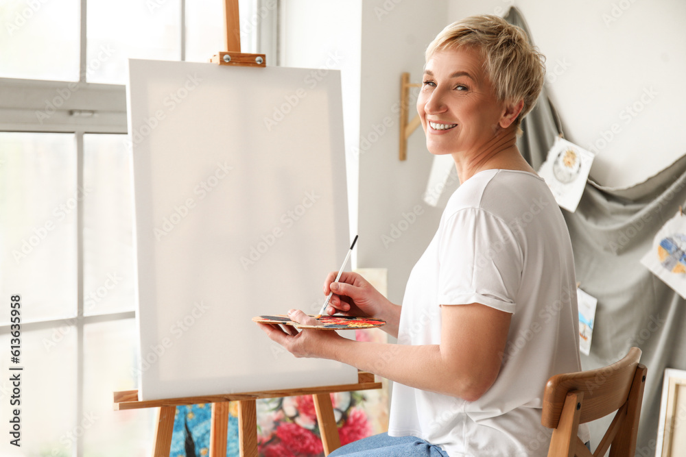 Mature female artist painting picture in  workshop