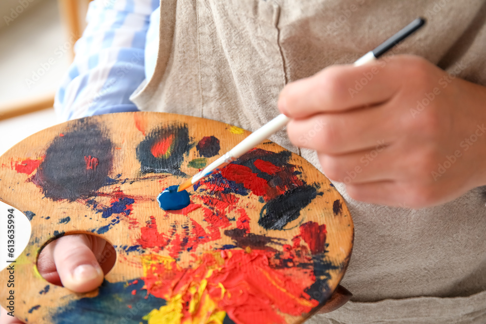 Mature female artist with palette and brush in  workshop, closeup