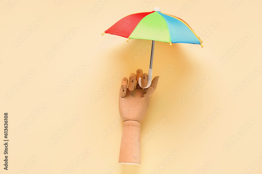 Creative composition with wooden hand and mini umbrella on pale yellow background