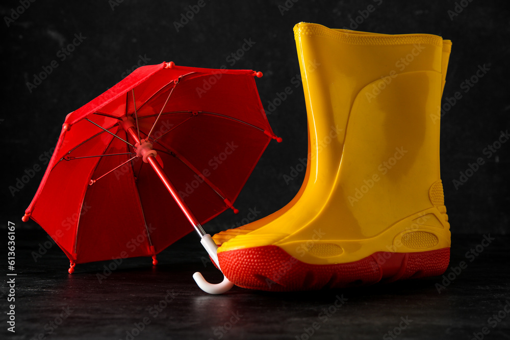 Gumboots and mini umbrella on black background