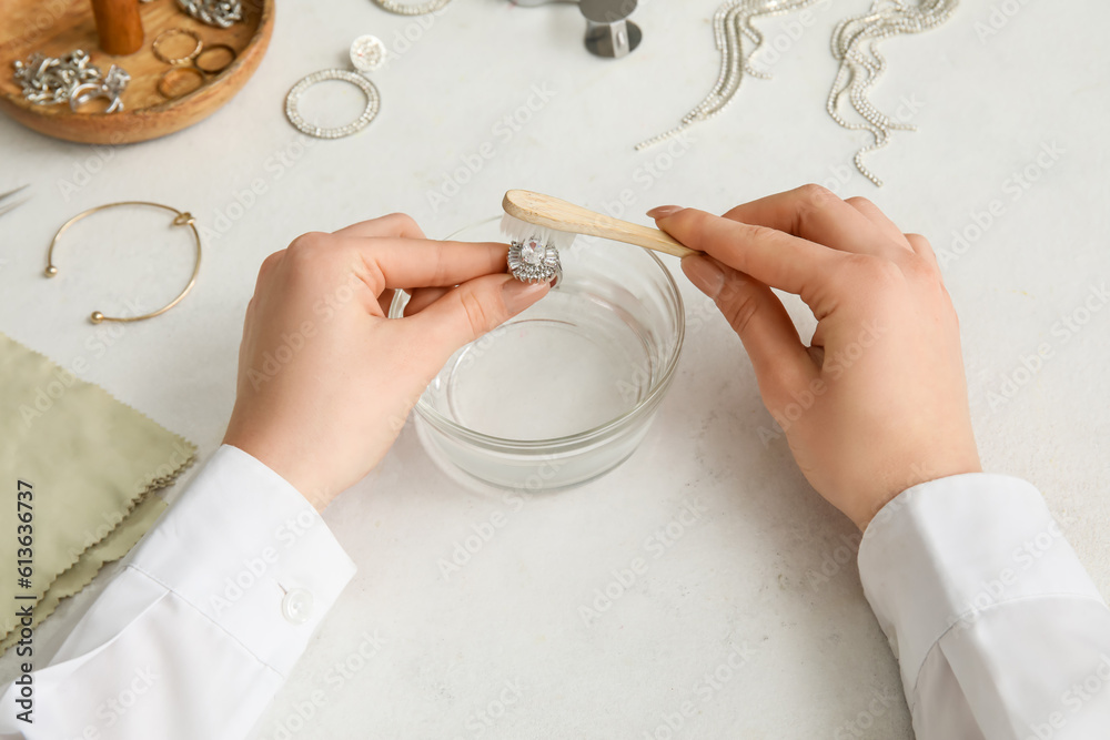 Woman cleaning beautiful ring with toothbrush on light background, closeup