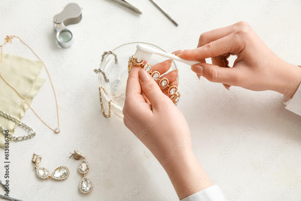 Woman cleaning beautiful bracelet with toothbrush on light background, closeup