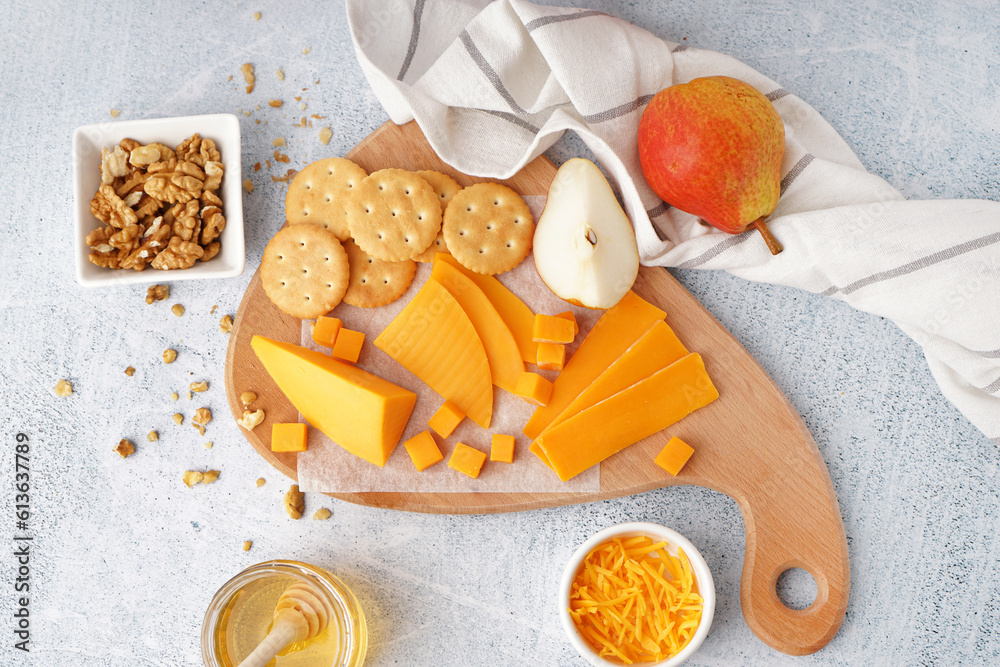 Board with tasty cheddar cheese, crackers, pear, nuts and honey on light background